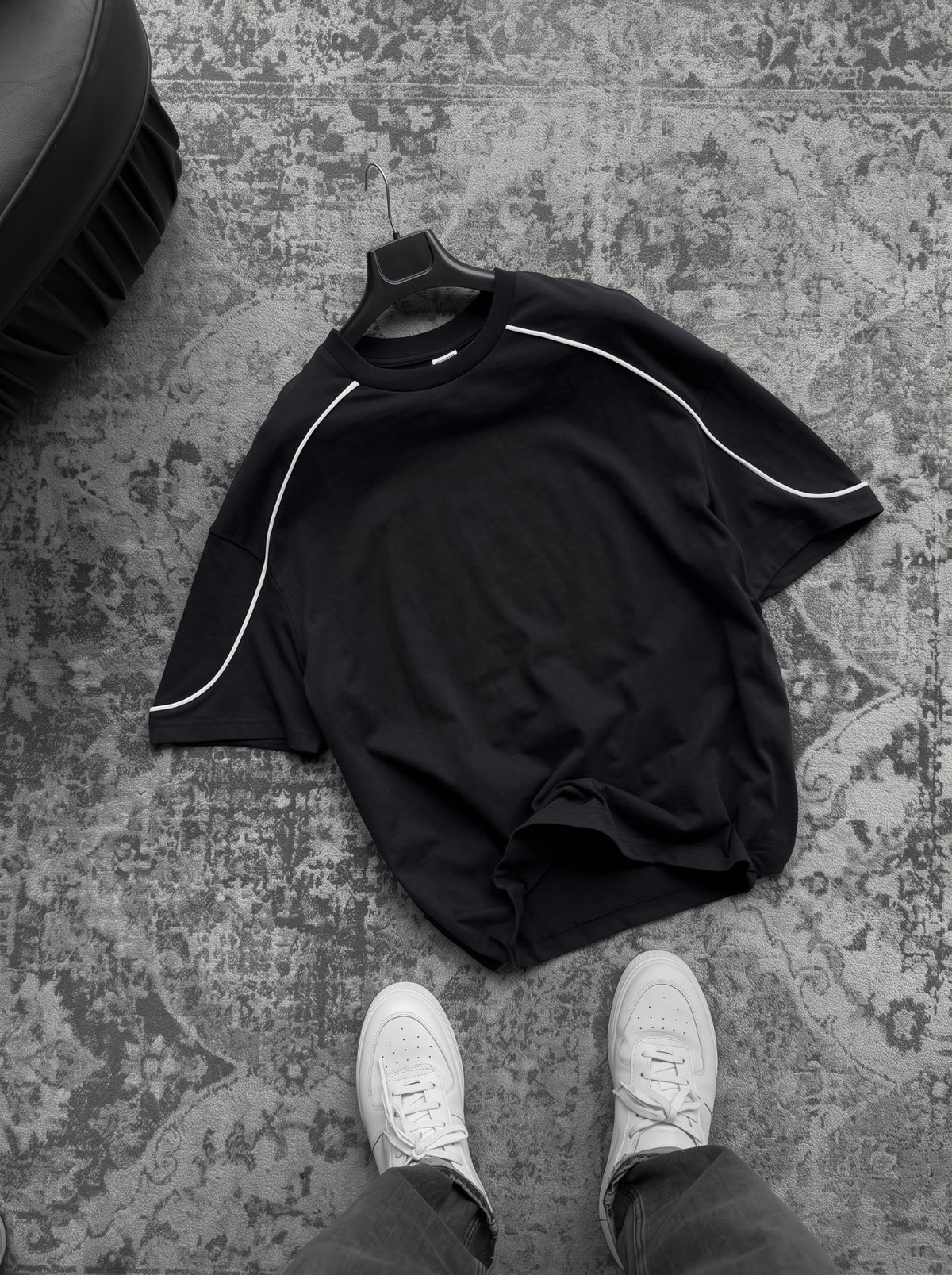 BROEK black oversized T-shirt on a hanger over a grey rug, with white contrast piping and a plain front.