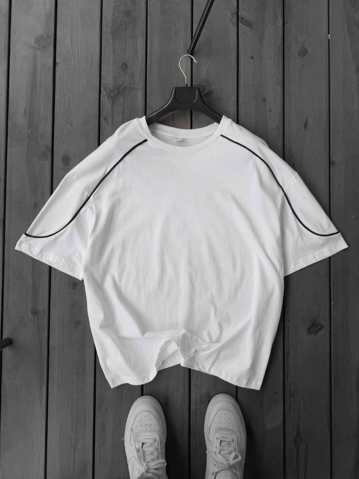 BROEK white oversized crew-neck T-shirt on a hanger, with curved black contrast piping across the shoulders and sleeves.